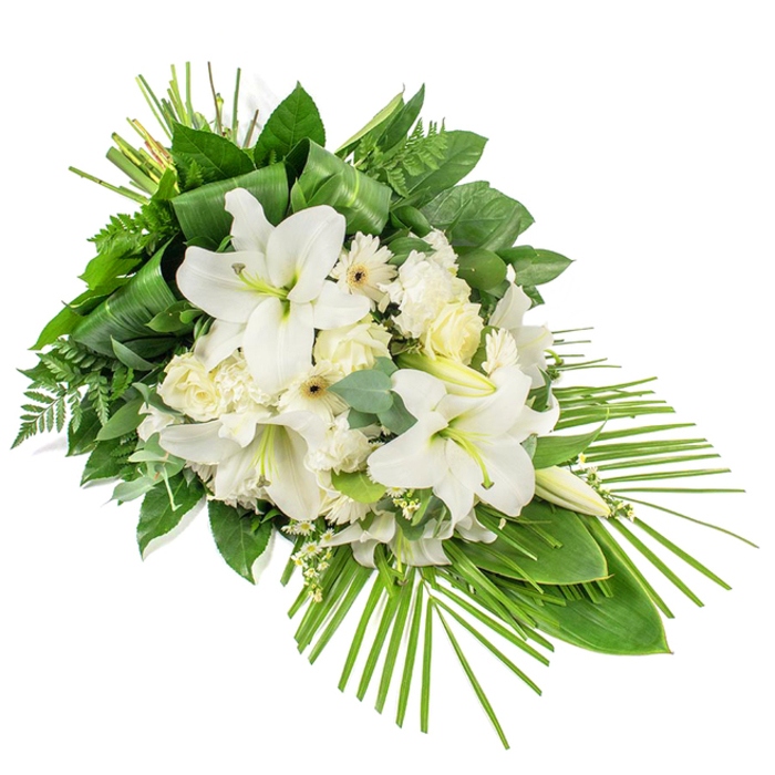 An elegant, long-stemmed funeral arrangement in pristine whites and lush greens is displayed diagonally across a clean white background, evoking the shape of a cascading teardrop or gently falling spray. The focal flowers are large white lilies, their broad, trumpet-like petals unfurled to reveal creamy centres and fine stamens lightly dusted with soft pollen, while several smooth buds stand nearby like quiet sentinels. Around them, white and cream roses are gathered, some tightly furled, others partially open, their overlapping petals creating a softly spiralled texture that speaks of grace and love. Ruffled white carnations fill out the design, their edges finely serrated and fluffy, adding both fullness and a comforting, familiar charm. Interspersed among these are white daisy-like blooms with pale yellow or cream centres, likely Gerberas or similar varieties, which lend a light, contemporary feel. Tiny clusters of white filler flowers are scattered throughout, giving the spray a delicate, almost ethereal layer. Supporting this is a rich bed of greenery: glossy dark green leaves provide a bold backdrop, feathery fern fronds soften the lines, and rounded eucalyptus leaves in muted green-blue shades bring subtle colour variation and a sense of calm. Along the top of the arrangement, long, narrow leaves are neatly wrapped and bundled, offering a sculptural accent, while from the lower right, slender palm fronds fan outward and trail away, emphasizing the elongated silhouette and giving the design a sense of gentle movement. The overall effect is tranquil and dignified, echoing the peaceful feel of Stanmore's tree-lined avenues and local chapels. This heartfelt floral tribute, thoughtfully designed for sympathy, memorial services, or graveside farewells, expresses purity, remembrance, and quiet support. Crafted with care by Flowers Stanmore, it reflects the sensitivity and respect local families seek at times of loss.