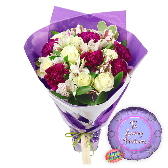 This photograph presents a polished graduation-themed bouquet and balloon ensemble against a bright white background, the kind of gift you might see waiting on a doorstep in Stanmore after results day. The bouquet dominates the scene, standing upright with a classic, tapered silhouette. Its stems are hidden behind layers of rich purple wrapping paper, which have been shaped into tidy, structured folds that cradle the flowers and rise gracefully behind them. At the base, a stylish green and white ribbon, possibly bearing a subtle pattern, is tied firmly, creating a decorative band that adds contrast and a hint of playfulness. Above this, the flowers themselves form a lush, rounded display. Several creamy white roses are dotted through the arrangement, their spiralled petals still fairly tight, suggesting they were cut at their prime. Between them, dense heads of deep fuchsia or magenta blooms-likely carnations or chrysanthemums-create bold islands of colour. Each bloom is made up of many ruffled petals, giving a sense of depth and movement, like waves of fabric in a graduation gown. Threaded delicately throughout are sprigs of tiny white filler flowers, which soften the transitions between the stronger colours and provide a light, airy texture. Fresh green foliage, in tones from bright to deeper emerald, frames and supports the blossoms, echoing the tree-lined streets and garden views around Stanmore's residential areas. To the lower right of the bouquet, resting on the same white surface, is a round purple Mylar balloon with a gentle metallic gleam. Its front is printed with the message To a Loving Graduate in flowing white script, the words curving along with the balloon's circular shape. Near it, a small oval tag or sticker featuring green and white details suggests a logo or quality mark from a local florist. The scene feels full of pride, joy, and affection, perfectly suited for celebrating academic success in Stanmore-from school leavers to university graduates.