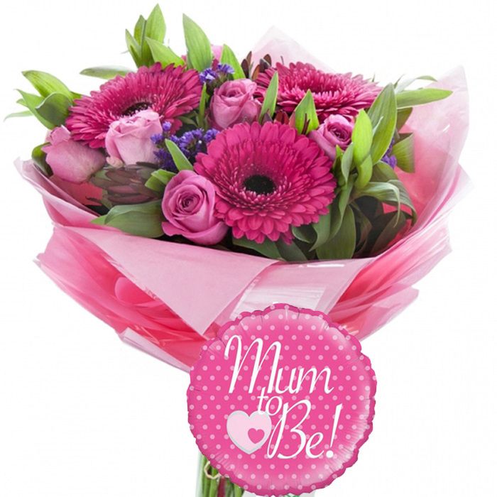 This image shows a charming Mum to Be floral gift set, carefully arranged against a spotless white background so every colour and detail stands out clearly. At the heart of the display is a lush bouquet built around several striking fuchsia gerbera daisies, their bold, dark centres surrounded by rings of finely textured petals that seem to glow from within. Nestled around them are pastel pink roses in varying stages of bloom: some remain as tight, promising buds, while others have started to open in soft, spiralling layers, like a gentle reminder of the changes ahead for an expectant mother. Threads of small purple filler flowers add a delicate mist of colour, giving subtle contrast to the pinks and enhancing the sense of depth. Glossy and matte green foliage weaves through the blooms, providing a fresh, natural frame that makes the arrangement feel as if it could have been gathered near Bentley Priory Nature Reserve and then refined by an expert florist. The stems are wrapped in layered pink tissue paper, from pale blush to brighter tones, gathered into a ruffled collar and sealed with an outer layer of clear, reflective cellophane that hints at professional presentation for delivery anywhere in Stanmore. In front of the bouquet rests a round foil balloon with a softly scalloped edge, finished in vivid fuchsia and sprinkled with evenly spaced white polka dots. Across its centre, the words Mum to Be! appear in flowing white script, accompanied by a white heart cradling a smaller pink heart, echoing the love growing within. The whole composition radiates happiness, making it a fitting gift for baby showers, hospital visits, or joyful pregnancy announcements around Stanmore.