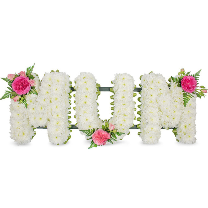 A lovingly designed funeral flower arrangement spells out the word MOM in large capital letters, set against a simple white background that allows the tribute to take centre stage. Each letter is shaped from a firm frame and is then entirely covered with masses of small white chrysanthemum heads. The chrysanthemums are arranged very closely, their numerous petals overlapping to create a plush, padded effect across the surface. The bright, clean white of the flowers echoes themes of purity and remembrance, and their rounded shapes introduce a comforting softness to the otherwise strong block lettering. At the very base of the letters, a narrow line of dark green-either a ribbon or the visible edge of the supporting stand-can be seen, giving gentle contrast and helping the word stand out with clarity. To soften the design further and to reflect a mother's warmth, three floral clusters in shades of pink are thoughtfully placed. One cluster adorns the upper left arm of the first M, where a striking fuchsia rose is surrounded by lighter pink spray roses and gathered with fine, serrated fern leaves. Another cluster nestles in the area between the lower curve of the O and the start of the last M, drawing the eye into the heart of the tribute, and the final group sits at the top right of the second M, completing the trio. The pink roses bring a touch of romance and gratitude, while the green ferns add airiness and movement. This MOM letter tribute would be a touching choice for funeral services and memorials around Stanmore, from local churches to quiet gatherings at the crematorium, offering a personal way to honour a much-loved mother. Families might picture it resting beside a photograph at a wake or placed gently on a coffin, a single word embodying years of love.