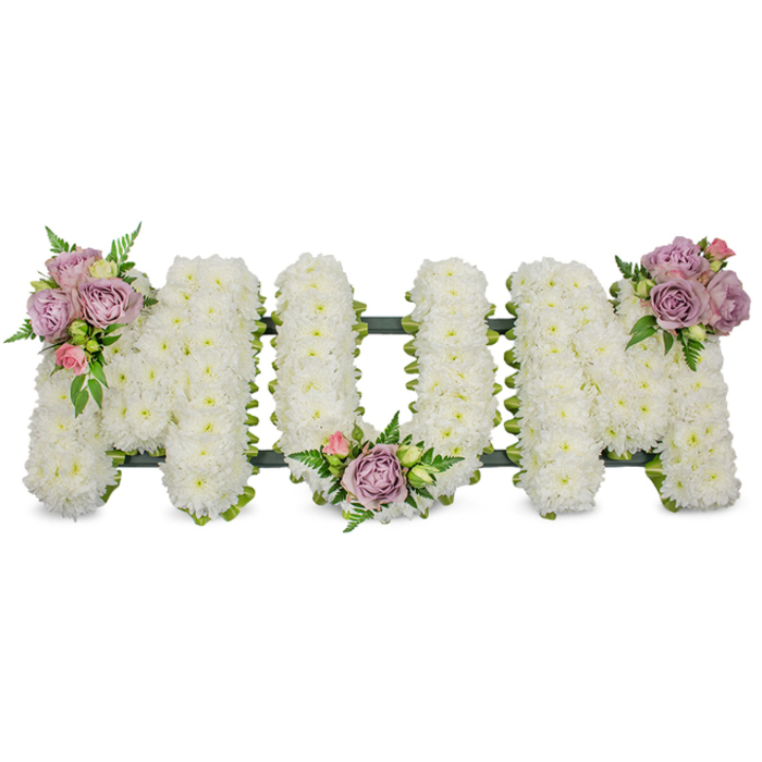 A striking, formal sympathy arrangement reads 'MUM' in bold capital letters, each letter meticulously cloaked in a dense carpet of small, white chrysanthemums to create a uniform, cushioned texture that appears almost luminescent against a clean, white photographic backdrop. The white heads are closely placed so the eye sees a continuous, soft surface; between them, the dark-green framework or ribbon-wrapped base shows faintly, offering structural definition and a subtle contrast that grounds the composition. Three refined accent groupings of delicate roses - pale lavender intermingled with soft pink buds - punctuate the display: one rising on the upper left limb of the first 'M', another nestled within the gentle hollow of the 'U', and the third adorning the upper right sweep of the last 'M'. Sprigs of feathery fern and fresh green foliage curl around the roses, their slender leaves adding texture and a cool colour note that balances the warm pastel blooms. Together these materials create a tactile story: the fluffy chrysanthemums speak of peace and remembrance, the velvety roses of tenderness, and the greens of life and continuity. The bouquet carries a subtle floral fragrance that is neither overpowering nor intrusive, appropriate for services and wakes, and the overall effect is one of thoughtful restraint and dignified remembrance. This bespoke tribute would sit respectfully at a funeral or graveside for a mother, conveying love, honour and lasting memory to family and friends gathering from Stanmore, Harrow and surrounding communities.
