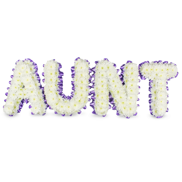 A meticulously arranged sympathy tribute spells out AUNT in large, confident capitals, each letter densely filled with small, immaculate white spray chrysanthemums. The chrysanthemums' many-layered petals create a soft, foamy surface across the letters; occasional pale yellow centres glimmer through the white masses like tiny points of light, adding natural detail and tenderness. Each letter is edged with a deep purple satin ribbon that has been gently gathered into ruffles and pleats, producing a refined scalloped border that contrasts the purity of the blooms and gives the letters an elegant finish. The construction sits slightly raised from the white surface, with subtle grey shadows beneath each form that illustrate the depth and solidity of the frames used to support the flowers. A mild, fresh scent of green stems and clean petals is suggested, enhancing the sense of quiet purity. Visually, the piece balances dignity and warmth, delivering a message of reverent love rather than solemn austerity - an accessible, consoling tribute for viewings or services in the Stanmore area, perhaps delivered to a chapel near Stanmore Park or placed at a community memorial service close to Canons Park. The careful packing of the chrysanthemums, the precision of the lettering and the thoughtful use of lavender-toned ribbon communicate professional workmanship and heartfelt intent: a personal memorial that honours an aunt's life with grace, clarity and softness.