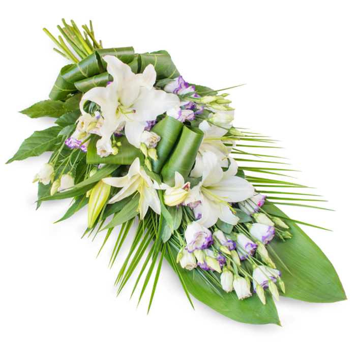 Photographed against a clean white background, this sophisticated funeral spray is arranged in a classic teardrop form, placed diagonally so the eye naturally travels from a rounded, full upper section down to a slender, elegant tip. At the heart of the design are several white oriental lilies, some fully open with large, trumpet-shaped petals that curl softly and reveal pale yellow-green stamens, others still enclosed as smooth, pale buds that soften the silhouette. Interlaced among these dominant blooms are clusters of lisianthus, their white, bell-shaped flowers delicately edged with a hint of lavender or light purple, with fine veins adding a touch of gentle colour to the otherwise serene palette. Numerous buds and partially opened lisianthus blossoms create layers and a sense of quiet movement. The entire composition is framed by abundant greenery: broad, dark green leaves provide a strong structural base and rich contrast against the white petals, while long, slender palm-like fronds sweep outward and down, accentuating the spray's flowing, elongated line. Some of the leaves are intricately rolled and folded, forming neat, sculptural details that speak to the care and skill of a florist from Flowers Stanmore, used to creating meaningful tributes for local services across Stanmore and nearby Harrow Weald. The overall atmosphere is one of peaceful dignity, reminiscent of the calm found in the gardens around Stanmore Country Park. This piece would be fitting for a casket top, a memorial stand, or a graveside tribute, offering a tender, refined expression of sympathy and remembrance for families gathering to say farewell.