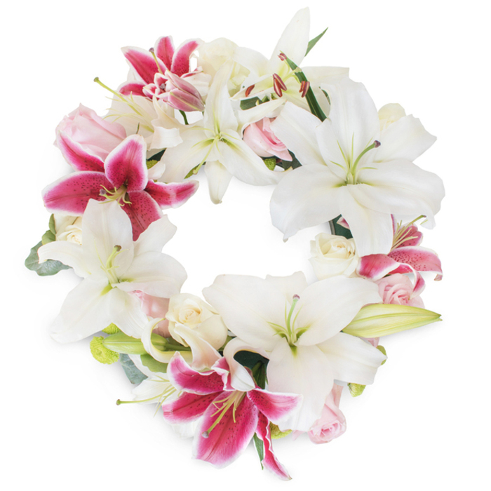 Against a clean, white backdrop, a luxurious circular funeral wreath commands attention-skillfully designed by Flowers Stanmore to embody both tradition and refined artistry. Dominating the arrangement are stately white lilies, with petals that arch gracefully outward in a captivating star formation, their pristine colour representing resilience and tranquility. Intertwined with these are vibrant fuchsia and deep pink lilies, adorned with subtle speckles and soft white edges, their striking presence bringing a sense of life and dynamic movement reminiscent of Stanmore's local flower markets. Nestled delicately among the lilies, blush pink and creamy white roses provide textural depth, their layered petals either just unfolding or held in delicate buds, symbolizing gentle remembrance and hope. Intermittent hints of fresh, muted greenery and small, button-like flower buds peek through, echoing the lush lawns and gardens that define Stanmore's residential streets. The ring of blooms forms a seamless, full circle, offering a sense of continuity and eternal connection-an ideal centrepiece for a celebration of life, funeral tribute, or a comforting gesture for a grieving family. With expertise honed by years serving Stanmore and nearby Belmont, each bloom is meticulously placed, ensuring this floral wreath elegantly honours a legacy and delivers solace to all who gather.