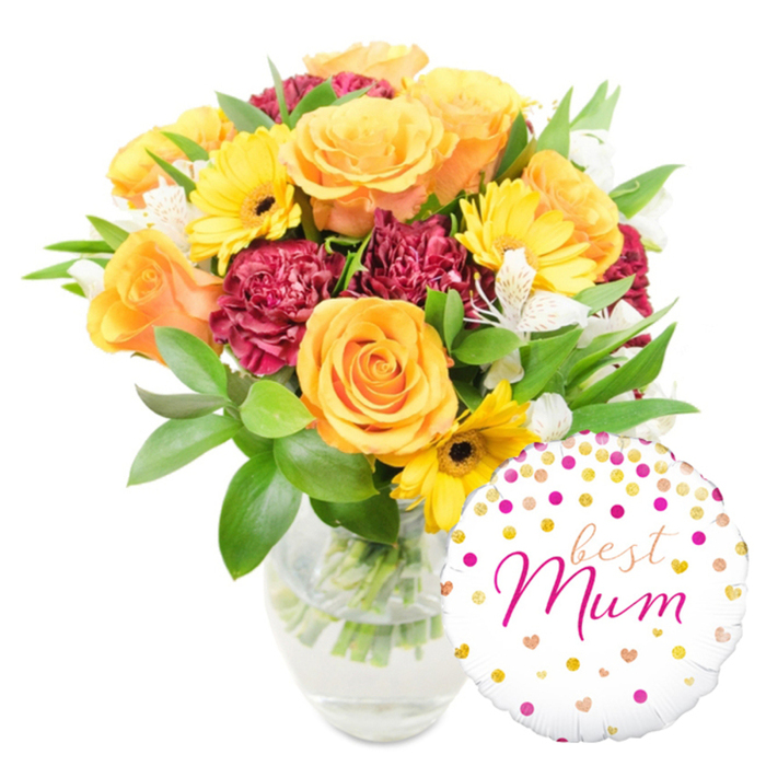 A celebratory, hand-styled bouquet in a simple clear glass vase, paired with a cheerful white foil balloon - an arrangement I would personally deliver around Stanmore Broadway, Canons Park and the surrounding streets. The composition balances warm, embracing tones with textured, botanical detail: peachy-orange roses, large and fully open, form a luminous centre whose velvety petals spiral outward; bright yellow gerbera daisies peek through like small suns, their dark centres offering a crisp graphic contrast. Deep burgundy carnations bring a lush, velvety density that anchors the arrangement visually, while slivers of white alstroemeria - slender, speckled and refined - soften the palette and introduce delicate rhythm. A generous variety of green foliage surrounds the blooms, from glossy, broad leaves that frame the bouquet to finer sprigs that add air and movement; the stems sit visibly in clear water, signalling freshness and careful preparation. The balloon, positioned low and to the right, is glossy white Mylar patterned with scattered gold and fuchsia confetti-like dots and little heart shapes; across its face an elegant fuchsia script reads best Mum, the typography both playful and affectionate. This is the kind of thoughtful gift many customers request for Mother's Day or a special birthday - a bouquet for a beloved mother that reads as warm, confident and garden-fresh. Flowers Stanmore arranges and dispatches combinations like this for same-day delivery across Stanmore, Queensbury and nearby Harrow, ensuring the blooms arrive as vibrant as they appear here.