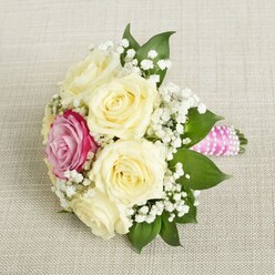 Imagine a bouquet crafted to capture the essence of Stanmore's graceful gardens in the first light of day-a gathering of creamy ivory roses, each bloom open and lush, embodying quiet sophistication. Resting gently on a pale woven fabric reminiscent of elegant table linens often seen at events hosted in Stanmore's stately homes, the bouquet forms an intimate cradle of plush roses. At its heart lies a striking magenta-pink rose, glowing with a jewel-like vibrancy, as if promising new stories along Stanmore's leafy streets. Encircling the blooms, clouds of white baby's breath weave in and out, lending the bouquet an ethereal touch similar to the mist over the nearby Common. Accents of deep green foliage peek from beneath the petals, anchoring the arrangement with a sense of natural composure and hinting at the verdant beauty found across Stanmore's parks. The stems are expertly wrapped in smooth, shimmering pink satin ribbon, with a spiral of luminous pearls adding a final note of refined charm. Whether destined for a wedding aisle or an intimate celebration, the bouquet whispers of joy and artistry nurtured within Stanmore, inviting the recipient to sense the fragrance of fresh roses, the crispness of greenery, and the loving hands that shaped each detail.