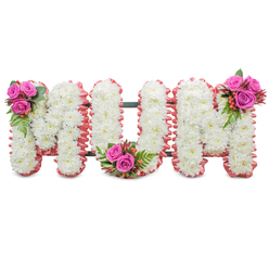 This carefully constructed MUM tribute reads like a quiet, loving message in flowers: three large, connected capital letters crafted primarily from tight clusters of pristine white chrysanthemums. The texture is soft and even, each tiny bloom contributing to an almost fabric-like surface that reflects light with a cool, dignified sheen. Around the outer edges a ruffled pale-pink trim-ribbon or soft fabric-frames the letters and introduces a delicate warmth that complements the white without overpowering it. A dark green support frame is visible where the letters meet, practical but discreet, holding the standing arrangement upright. Accenting the composition are three compact bouquets of vivid fuchsia roses placed with care-one at the top left of the first M, one tucked into the base of the U, and one crowning the top right of the final M-each accompanied by fern-like greenery and clusters of reddish-orange hypericum berries for contrast and depth. The overall scent is subtle: the powdery chrysanthemum undercurrent softened by the velvety perfume of roses. As a Stanmore florist I would imagine this tribute being ordered for a wake at a nearby chapel off Stanmore Broadway or delivered to family homes around Cannons Park; the makers at Flowers Stanmore craft it to convey respect, love, and remembrance with restrained elegance. The arrangement feels both traditional and personal, offering a visual language of purity in the white mums and affectionate warmth in the pink roses-a composed farewell suitable for a mother remembered with tenderness.