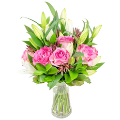 An elegant, vibrant arrangement of fully opened deep pink roses and poised white lily buds rests in a transparent glass vase, presented against a pristine white backdrop so each texture and hue is unmistakable. The roses form a plush central cluster, their velvety petals ranging from soft blush to intense fuchsia, layered like silk and softly reflecting the room's light. Tall white lilies rise through the composition, some still in tight green-tipped buds and others just unfurling to reveal creamy trumpets and the faint dusting of pollen on their stamens, suggesting a delicate floral perfume. Lush greenery - glossy broad leaves and finer, lighter fronds - surrounds and supports every bloom, creating a full dome that balances colour and form; small pockets of darker reddish-brown filler add sculptural punctuation and a hint of autumnal warmth. The vase's slightly tapered base and clear water show the trimmed green stems, a detail that signals freshness and care. This arrangement feels both joyful and refined, perfect as a gift for a special occasion or a calming focal point in a living room after a stroll near Canons Park. As a local Stanmore florist I imagine it being prepared in our shop window on Stanmore Broadway and offered for same-day delivery across Stanmore and nearby Harrow by Flowers Stanmore, where craftsmanship and neighbourhood knowledge matter.