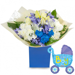 A tender, celebratory floral composition presented in a deep royal-blue rectangular box, arranged to welcome a newborn son with classic grace. The bouquet centers on soft white roses and round, cushiony white chrysanthemums, their petals layered like miniature clouds, while long white lilies-some still in tight buds-lift the arrangement with quiet, architectural elegance and a faint, sweet fragrance. Electric-blue chrysanthemums provide a vivid focal point, their saturated colour echoing the distant blue of a spring sky, and sprigs of pale lavender or periwinkle hyacinth-like flowers weave through the design, offering delicate texture and a cool, restful contrast. Rich green foliage-broad leaves and feathery fern tips-creates a verdant backdrop and breathes life into the sculpted shape. Around the stems, crinkled cream tissue provides a soft, tactile finish that complements the box's matte surface. To the right, a light-blue foil balloon in the shape of an old-fashioned pram shines with a polished glow; darker-blue accents on the canopy and wheels, tiny heart motifs, and the cheerful yellow-and-green "It's a Boy" lettering make the announcement unmistakable. Soft daylight captures the subtle sheen of petals and the metallic shimmer of the balloon, giving the set a calm, celebratory warmth. As a local florist would arrange for a new arrival in Stanmore-ideal for hospital ward visits, baby showers, or home welcomes near Marsh Lane and Stanmore Broadway-this floral-and-balloon gift reads as thoughtful, fresh, and immediately ready for delivery in the Harrow area.