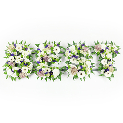 An intimate, overhead composition spells 'DAD' in a soft tapestry of whites, purples and greens, arranged with the thoughtful restraint you expect at a funeral or remembrance service. The three letters are densely packed with velvety chrysanthemums, large ivory gerbera blooms and pastel coffee-toned roses whose gentle warmth complements the cool whites. Small clusters of violet statice and deeper mauve fillers thread through the layout, giving a subtle playful depth that eases the formality of the tribute. Fern fronds trace each letter's edge in crisp, living green, their serrated silhouettes framing the petals and adding movement, while compact green button chrysanthemums are nestled throughout to punctuate the composition with fresh, rounded texture. The blooms sit upon a discreet dark base that contours the letters, visible here and there and offering structural contrast that keeps the message clear from a distance. In the soft studio light the petals hold highlights and shadow, suggesting a tactile softness and the faint, comforting scent of freshly opened flowers. As a Stanmore florist who has prepared many family tributes for services near Stanmore Broadway and Bentley Priory, Flowers Stanmore often chooses this palette to convey steady affection and respect-it reads as sincere and quietly celebratory of a life. The overall effect is both composed and compassionate: a tangible, floral embrace when words fall short, ready to be placed beside a service or chapel tribute.