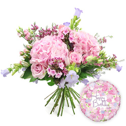 A lavish birthday bouquet in soft pinks, lilacs, and fresh greens is captured against a pure white background, giving every bloom space to shine. At its heart, generous heads of blush pink hydrangea create full, rounded cushions of petals, each one contributing to a sense of indulgent abundance and romance. Nestled between them are elegant soft pink roses; some are fully open with their petals unfurling in classic spirals, while others remain as neat buds that will slowly open over the next few days, extending the life of the arrangement. Threaded throughout are dainty clusters of vibrant fuchsia waxflowers, or a similar tiny filler flower, lending fine texture and pops of deeper colour that feel reminiscent of the flower-rich hedgerows around Stanmore and nearby Bushey. Tall, slender stems of campanula rise gracefully from the bouquet, tipped with delicate bell-shaped blossoms in lavender and periwinkle, adding a cool contrast to the warm pinks and drawing the eye upwards. Surrounding this mix of blooms, a variety of lush green foliage-some leaves broad and glossy, others slim and arching-softens the edges and frames the flowers in natural richness. The stems are clearly visible at the bottom, gathered neatly in the classic hand-tied style favoured by local Stanmore florists, ready to slip into a vase as soon as they arrive. Positioned to the lower right, a glossy round foil balloon completes the celebratory look. It is patterned with tiny roses and buds in shades of pink, lilac, and cream, echoing the bouquet's colour story, while in the centre, the words "Happy Birthday" appear in an elegant purple script. This harmonious pairing of flowers and balloon creates a complete birthday gesture, perfect for surprising someone special at home or work in Stanmore.