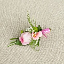 Illuminated by soft daylight, a finely designed floral boutonniere lies gently on an oatmeal-toned, textured background, echoing Stanmore's blend of tradition and modernity. The focal rosebud, pale pink and tightly woven, exudes a quiet grandeur-its spiral petals promising freshness and poise. Nearby, a petal-soft flower in light peach-pink, likely Alstroemeria, unfolds with subtlety, its center glowing with gentle yellow and unique flecks reminiscent of wildflowers in local meadows. Fleecy clusters of tiny white baby's breath offer an airy softness, while button-like bursts of vibrant green mums lend a joyful burst of colour, reflecting the life found in Stanmore's lush parks and leafy avenues. Dark, spiky greenery creates upward movement and structure, complemented by wide, elegantly folded leaves that secure the arrangement and evoke a sense of stability and grace. A shining fuchsia pink satin ribbon, wrapped snugly at the boutonniere's base and fashioned into a tidy bow, injects energy and festive brightness-perfect for the cheerful atmosphere of local weddings and events. Each flower and leaf is arranged with precision-the hallmark of experienced local craftsmanship. Ready to adorn a groom's lapel or act as a finishing touch for a Stanmore celebration, this boutonniere's gentle hues, fresh textures, and artisan binding speak of romance, hope, and the refined style appreciated throughout the area.