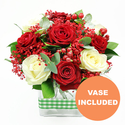 In this image, a thoughtfully arranged bouquet stands out vividly against a plain white background, its rich colours and textures suggesting a moment of celebration in Stanmore, perhaps after a stroll through Canons Park. Luxurious red roses dominate the arrangement, their velvety petals unfolding in generous layers, mingling with creamy white roses that add a softer, more tranquil note. These contrasting hues create a romantic interplay of light and shadow across the blooms. Delicate clusters of tiny bright red filler flowers are tucked among the roses, softening the transitions and adding a feathery, almost cloud-like touch that gives the whole design a sense of airiness. Glossy red hypericum berries scatter through the bouquet like polished beads, introducing rounded shapes and extra points of rich colour. Framing the roses is an abundance of fresh greenery: eucalyptus sprigs with subtle silvery-blue undertones and other leafy stems in deeper greens, which give structure, fullness, and a natural garden feel reminiscent of local Stanmore greenery. The flowers are arranged in a sleek, clear rectangular glass vase; the visibility of the stems and the clean geometric lines lend a contemporary edge that would look at home on a dining table along Marsh Lane or in a light-filled Stanmore apartment. Around the midsection of the vase, a green and white gingham ribbon is wrapped in a smooth band, adding a rustic, homely charm that balances the bouquet's sophistication. In the lower right corner of the photograph, an orange circular icon displays the words "VASE INCLUDED" in crisp white text, indicating that this floral gift is complete and ready to display, an ideal choice for birthdays, anniversaries, Valentine's surprises, or simply brightening a loved one's day in Stanmore with fresh, professionally arranged flowers.