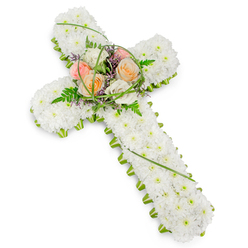 Against a spotless white backdrop, this traditional Christian funeral cross stands out with quiet strength and refinement. Its entire surface is densely dressed in small white chrysanthemums, each bloom carefully set so that they touch and overlap, forming a continuous, cushion-like texture with no visible gaps. The sea of white petals evokes purity and a sense of stillness, like a moment of silence held in a church near Stanmore Broadway. Running around the full perimeter of the cross is a slender border of fresh green foliage and floral edging, tracing the silhouette with a clear, defined line and bringing in the calm energy of living greenery. At the heart of the design, where the horizontal and vertical beams meet, sits a raised spray that draws the eye. A cluster of roses in gentle shades of peach, apricot, blush pink, and creamy ivory is arranged so that their spiralling centres face outward, symbolising tenderness and affection. Interspersed among the roses are airy fern fronds, looping strands of bright green grass, and dainty purple filler flowers, which lend the piece texture, depth, and a touch of understated colour. The lighting is bright yet soft, allowing each detail of the flowers to be clearly seen without harsh contrast. This tribute feels perfectly suited to a Stanmore funeral or memorial gathering, whether resting atop a coffin in a chapel, placed beside a lectern for a service of thanksgiving, or laid gently at a graveside. The cross communicates faith, remembrance, and the quiet promise of eternal rest through its thoughtful, carefully balanced floristry.