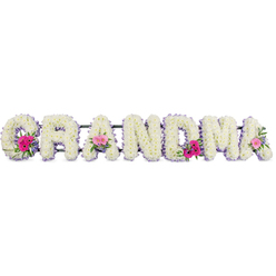 This image features a heartfelt floral tribute where the word "GRANDMA" is formed by bold block letters, each completely coated in crisp white chrysanthemums. The chrysanthemums are carefully arranged so that their small, layered petals create a plush, even surface, resembling a soft cushion of bloom upon bloom. A slim border of lilac ribbon traces the outline of every letter, its gentle pastel shade and smooth, satin finish adding a refined touch and a hint of colour that feels both soothing and respectful. The letters stretch across the frame on a concealed support, echoing how they might rest at a funeral or memorial service in Stanmore, perhaps at a local church or crematorium serving families from around Marsh Lane, The Broadway, and beyond. At three points, the flow of white is softened by small, rounded clusters of mixed flowers. Set on the opening "G", one of the central "A"s, and the final "A", these posies combine vibrant pink gerbera daisies, with their clear, circular centres and bright, radiating petals, and blush-pink roses whose velvety petals gently unfurl from tight centres. Sprigs of fresh greenery weave through these accents, introducing natural curves, deeper green tones, and a sense of movement. The light is soft and balanced, free from harsh shadows, so that every detail of petal, leaf, and ribbon edging is gently illuminated. No vase or additional decoration is visible, keeping the focus on the floral lettering itself. The overall impression is of a loving, bespoke farewell, a floral expression of gratitude and remembrance for a grandmother whose influence and kindness are fondly remembered.