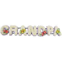 Set against a plain white studio background, this dignified floral tribute forms the word GRANDPA in bold capital letters, designed with the quiet elegance you might expect from an experienced Stanmore florist. Each block-style letter is built on a sturdy frame and densely covered in small, pristine white chrysanthemums, their rounded petals packed so closely that the surface appears like one soft, continuous cushion of bloom. The uniform sea of white suggests purity, peace, and the comforting presence of family gathered to say goodbye. Skimming along the base of each letter is a trim of soft lavender ribbon, visible as a narrow band of pale lilac that subtly outlines the forms and adds a gentle, almost spiritual wash of colour. The letters sit in a straight row on dark green bars, which barely show but ensure the tribute remains aligned and easy to display on a hearse or at the front of a chapel in Stanmore. Carefully placed sprays of more vivid flowers break the white expanse, like cherished memories standing out in the mind. On the G, a lush cluster of deep red anthuriums, their waxy, heart-shaped spathes gleaming under the light, is framed by glossy green leaves. The first A carries an elegant arrangement of yellow-green orchids, their delicate petals and speckled throats giving a sense of grace and enduring beauty. The central D mirrors the G with more crimson anthuriums and foliage, creating a visual rhythm through the tribute. The final A repeats the soft yellow-green orchids, balancing colour and form from left to right. This personalised GRANDPA design is created as a heartfelt funeral or memorial tribute for families in Stanmore, expressing love, gratitude, and remembrance through thoughtful floral artistry.