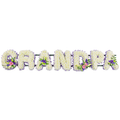 This floral arrangement presents the word GRANDPA as a graceful funeral tribute, with each of the seven capital letters made entirely from fresh white blooms. The letters stand in a neat line on a slender dark green frame, which runs horizontally behind them and keeps the word perfectly aligned. The main body of every letter is densely covered in small white chrysanthemums or similar multi-petalled flowers, giving a soft, cushioned look that suggests gentleness and purity. Around the perimeter, a narrow trimming of lilac and pale purple flowers carefully follows the shape of each character, providing a cool, pastel outline that enhances the readability of the name without introducing harsh contrast. Throughout the tribute, the florist has woven in several accent clusters that feel personal and expressive, like small floral stories about the grandfather being honoured. On the G, an elegant white lily-style flower opens above rich pink and fuchsia blooms, all nestled in glossy green leaves. The first A carries a more modest bouquet of pink and purple tones, while the D features a more prominent spray, again mixing white lilies, bright pink flowers, and fresh greenery. Another A bears a smaller cluster, and touches of green button chrysanthemums appear in places, adding spots of lively green to the composition. Photographed against a clean white background with soft, even lighting, every petal and leaf is clearly visible, showcasing the thoughtful craftsmanship. This is the kind of tribute a family in Stanmore might choose for a beloved grandfather's service at a local crematorium, synagogue, or church, perhaps after a quiet walk through Canons Park or along Stanmore Hill, bringing a sense of peace, remembrance, and enduring affection.