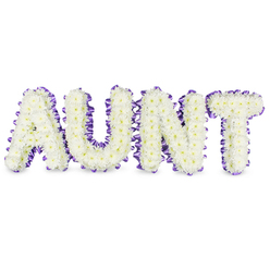 As a florist who works in and around Stanmore, I describe this design as a personal, reverent statement: the word "AUNT" sculpted in bold capital letters, each letter densely composed of hundreds of small, pristine white spray chrysanthemums. The chrysanthemums create a plush, cloudlike texture across each letter's surface, their tiny petals overlapping like silk; here and there the pale yellow centres of individual florets add a whisper of warmth, keeping the white from feeling stark. Around the perimeter of every letter runs a deep purple satin ribbon, ruffled and pleated to give a soft, scalloped edge that both frames and elevates the flowers; the ribbon's satin catch subtly reflects chapel lights or the diffuse daylight of an overcast Stanmore afternoon. Grey shadows beneath the letters reveal their dimensional frames and separate them gently from the white backdrop, making the tribute read clearly from a distance at a service. There is a quiet vegetal scent, clean and green, and an overall impression of calm, respect and love. This is the sort of bespoke memorial piece we prepare with care at Flowers Stanmore for families who want a named tribute that is both traditional and quietly uplifting - suitable for display at funerals near Stanmore High Street, in small community memorials or placed with other floral tributes at home viewings. The arrangement's balance of texture, colour and form offers solace, a handcrafted emblem of remembrance.