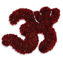 A handcrafted floral tribute shaped into the sacred Om symbol, assembled from densely packed deep-red chrysanthemum blooms, conveys a quiet, contemplative reverence. Each swirl and curve of the symbol is formed from hundreds of small, button-style chrysanthemums whose petals offer a velvety, garnet-red surface; tiny bright-green centers peek through in places, adding delicate points of contrast that animate the contour. The blooms are so closely set that the symbol reads as a plush, tactile object - soft to the eye and suggesting the faint, earthy scent of fresh chrysanthemums when imagined close up. The composition sits on a spotless white background, the starkness of which sharpens the Om's silhouette and focuses attention on the care taken in every curve. A subtle, diffused gray shadow beneath the arrangement lifts it just slightly from the surface, giving a sense of weight and quiet elevation as if the offering were resting on a shrine table in soft morning light. The piece feels entirely appropriate for a moment of solace, a memorial ceremony, or a meditative gathering in and around Stanmore's quieter corners - perhaps near Canons Park or a local chapel - where floral offerings are used to hold space for mourning and healing. The craftsmanship speaks of a florist accustomed to sensitive commissions: measured, respectful, and deeply rooted in the traditions of comfort and remembrance.
