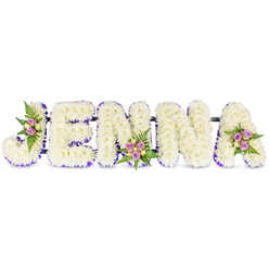 This personalised sympathy tribute reads JENNA in sculpted, three-dimensional letter forms set on a pristine white field. Each letter is compactly formed from an abundance of small, snow-cream chrysanthemums or similar tiny florets, creating a soft, pillowy texture that invites a gentle touch in the mind's eye. A delicate ribbon-like border of rich purple trims the inner edges of each character, accentuating the silhouette and introducing a calm, dignified colour note. Three tasteful floral clusters break the white plane: one arranged into the inner curve of the J, another positioned on the second N's lower centre, and a final grouping adorning the top curve of the A. Those clusters combine blush and lavender spray roses with a scattering of pale cream-yellow roses and fresh dark-green fern fronds, the contrast of textures adding both warmth and botanical life. The letters are subtly linked by slim, dark structural bars that keep the tribute aligned for display at a wake or graveside service. Light is soft and even across the arrangement, picking out the chrysanthemums' tiny petals and the roses' layered cups while preserving an atmosphere of quiet dignity. As made by a local florist sensitive to memorial needs, this floral name piece conveys reverence and memory - a personal focal tribute suitable for funerals in the Stanmore area, from chapel services near Canons Park to intimate gatherings on Stanmore Hill.
