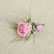 Resting on a softly textured, pale beige cloth that resembles fine linen, this pink rose boutonniere captures the quiet elegance often chosen for weddings and formal events around Stanmore. The eye is immediately drawn to the single rose, placed slightly diagonally in the lower left portion of the image, its petals arranged in an intricate spiral that feels both natural and meticulously tended. The colour deepens at the outer edges into a velvety magenta, then gradually transitions to a lighter blush, ending in a pastel pink centre that seems almost luminous against the neutral background. Framing the rose, delicate sprigs of white baby's breath appear like tiny constellations, softening the form and adding gentle contrast. Slender, green, grass-like stems reach out from beneath, their fine lines echoing the gentle curves you might notice in the greenery of Bentley Priory Nature Reserve. At the base, a broader dark green leaf is carefully curled around the stems, forming a smooth collar that both supports the flower and accentuates its shape; small beads of water cling to the leaf, giving the impression that the piece has just been misted and is ready for same-day use. The stems themselves are wrapped tightly in a pale pink satin ribbon, the texture smooth and slightly reflective, and this is finished with a narrow, darker magenta bow tied precisely at the bottom. The lighting is soft and even, enhancing the rose's gentle glow without harsh shadows. This boutonniere feels designed for a groom's lapel at a ceremony near Stanmore station, a best man at a local synagogue wedding, or a prom attendee looking for a refined floral accent that quietly conveys romance and thoughtful preparation.
