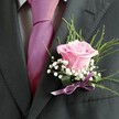 There's an unspoken elegance in this buttonhole, a poem written in petals that reflects the warmth of Stanmore gatherings. At its core, a blush-pink rose presents its velvety folds, each one opening as if in anticipation of promises exchanged in the gardens near Stanmore Hill. The scent is tender and subtle, whispering of new beginnings and sunlit celebrations. Dewy tufts of baby's breath surround the rose, their white faces lending a cloud-like softness that illuminates the arrangement. Slender green stems arc gracefully, invoking a feeling of freshness and movement inspired by mornings at Bernays Gardens. Set against the crisp lapel of a charcoal jacket and paired with a lilac-satin tie, the whole design glimmers under gentle daylight, secured by a silky lavender ribbon. Here, tradition and artistry blend-the boutonniere becomes more than an accessory; it is the finishing touch for moments of joy and connection, whether at a Stanmore wedding or a local celebration of friendship and family. In every detail, there is intention, skill, and a sense of belonging.