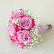Resting on a pale beige, textured fabric that resembles finely woven linen, this hand-tied bouquet showcases the artistry of a local Stanmore florist. The arrangement is intimate in scale yet rich in detail, led by several striking bi-colour roses. Each rose unfurls with a velvety softness, beginning with cool lavender or lilac tones in the centre and transitioning seamlessly into deeper magenta and fuchsia at the outer edges of the petals. The effect is that of a gentle watercolour wash, with colours blending smoothly in a way that evokes soft evening light over Stanmore's leafy streets and gardens. Between these dramatic blooms, clusters of white baby's breath create a delicate, misty frame. The gypsophila's tiny blossoms, no larger than pins, gather into little clouds that lighten the look of the bouquet, introducing a sense of airiness and traditional romance such as one might associate with bridal parties leaving a Stanmore church or registry office. The stems are drawn together tightly and wrapped in a rich, deep purple satin ribbon, whose smooth surface catches the light with a subtle sheen. Spiralling over the ribbon, a string of small white faux pearls traces a gentle curve, adding an elegant, almost vintage touch, as though a cherished piece of jewellery has been incorporated into the design. Placed at a diagonal angle with the pearl-wrapped handle pointing right, the bouquet feels poised and ready to be held for wedding portraits at Bentley Priory Museum, a milestone birthday celebration, or an intimate proposal. Overall, the image conveys refinement, careful attention to colour and texture, and the quiet excitement of a special day about to unfold in Stanmore.