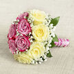 Placed gracefully on a pale, oatmeal-coloured cloth with a lightly textured, woven finish, this hand-tied bouquet commands attention through its balanced shape and thoughtful use of colour. From above, the bouquet appears as a rounded dome of roses, almost evenly divided into two contrasting yet harmonious halves. On one side, sumptuous fuchsia and magenta-pink roses bloom in full glory, each petal velvety and richly saturated, creating the impression of depth and romance you might associate with a sunset walk near Stanmore's leafy avenues. On the other side, a cluster of creamy, light yellow roses introduces a softer, more tranquil note, their gently layered petals glowing with a buttery warmth. Between these larger blooms, clusters of white baby's breath weave delicately, like fine lace or a veil of tiny stars, adding texture and an undeniably bridal feel. Subtle glimpses of deep green foliage break up the expanse of colour, providing contrast and reinforcing the sense that the bouquet is freshly assembled by an experienced florist. The stems are neatly trimmed and tied together, forming a practical handle that is carefully wrapped in smooth, shimmering pink satin ribbon. Around this ribbon, a narrow spiral of tiny white pearls is wound in even loops, combining simplicity with luxurious detail, reminiscent of a cherished piece of family jewellery worn for weddings in Stanmore. The overall impression is one of timeless romance and quiet sophistication, ideal for a church service, registry ceremony, or anniversary celebration within the local community, where the artistry of a dedicated florist turns flowers into keepsake memories.