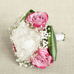 On a soft, off-white linen surface that looks like a carefully arranged piece of bridal fabric, a compact yet luxurious bouquet is captured from above, allowing every bloom to be clearly seen. The central focus is a plush creamy white peony, its petals tightly layered and slightly ruffled, forming a rounded, pillow-like bloom that radiates quiet elegance. Framing this peony are two richly coloured pink roses, thoughtfully positioned-one just above and one just below the centre. These roses reveal swirling hearts that open outward into petals tinted with gentle blush at the core and intensifying to vivid fuchsia tones at the edges, bringing a romantic vibrancy to the design. Interlaced among them are fine sprays of white baby's breath, their clouds of tiny blossoms adding lightness and a lace-like texture that seems to float around the more substantial flowers. The bouquet is cradled by wide, glossy dark green leaves that fold around its base, their smooth surfaces and deep hue providing a strong visual anchor. Beneath the foliage, the stems are trimmed evenly and bound in a sleek white satin ribbon, wrapped smoothly for a secure and comfortable grip, as if prepared for a bride leaving a Stanmore church service or stepping into wedding photos near Stanmore Country Park. The lighting is gentle and natural, enhancing the soft ivory tones, bright pink accents, and fresh greens without glare. The overall feeling is one of classic, understated romance, making this arrangement perfect for bridal bouquets, anniversary gifts, or editorial features on elegant wedding flowers crafted by experienced Stanmore florists.