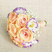 Captured in soft natural light on a pale, linen-like backdrop, this bouquet is an exercise in gentle contrast and tactile detail. A cluster of velvety apricot-peach roses forms the visual core, their petals tightly spiraled at the center and opening outward in warm, blushing layers that read as both plush and graceful. Interspersed among them, white lisianthus edged in lilac-violet provide a cool, contemporary outline; the ruffled edges and tiny yellow stamens bring delicate definition to each bloom. Wisps of baby's breath drift through the arrangement, tiny white orbs that create an ethereal veil and allow each focal flower to breathe. The handle is wrapped in a blush ribbon that mirrors the roses' tone, finished with neat rows of cream pearls for a quietly luxurious touch; at the very base, trimmed green stems remind you of fresh-cut workmanship. The composition sits slightly askew in the frame, photographed from above to show depth, texture, and the expert placement of each stem. There is an understated fragrance-light floral sweetness-that evokes early deliveries along Stanmore Broadway and the simple beauty of local gatherings. This bouquet feels especially suited to intimate weddings, anniversary gifts, or milestone celebrations held near Stanmore Hill or the local parish, where soft pastels and refined detailing complement a tranquil neighbourhood ethos.