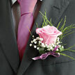 Pinned carefully to a dark suit jacket, this blush-pink rose boutonniere brings a feeling of tenderness and polished elegance to a special day in Stanmore. The rose itself is exquisitely formed, each petal smooth and velvety, overlapping in a soft spiral that draws the eye inward toward the gently cupped centre. The colour is a delicate blend of pale blush and creamy undertones, suggestive of early morning light over Stanmore Hill. Surrounding the bloom, airy clusters of white gypsophila, often known as baby's breath, create a cloudlike frame; their minuscule flowers scatter tiny highlights of white that stand out crisply against the dark lapel. Slender strands of greenery - trim leaves and graceful, slightly arching fronds - add just enough structure and natural movement to give the boutonniere a garden-fresh feel, as though it could have been gathered from a quiet corner of a local park. The stems are tightly bound in a satin ribbon of soft mauve or lilac, its subtle shine catching the light when the wearer moves, mirroring the gentle polish of dress shoes and cufflinks. The lighting in the image is comfortable and warm, casting light shadows that emphasise the rose's layered form and the texture of the surrounding foliage. This boutonniere would suit a groom, best man, or prom guest attending a celebration in Stanmore's churches, function rooms, or family homes, adding a discreet yet meaningful floral detail. Every line of wiring and ribbon work is clean and precise, reflecting a florist's practiced hand and the desire to create a small but unforgettable floral accent for moments filled with joy and promise.