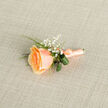 In soft natural light that might filter through the windows near Stanmore Broadway, a single peach rose is presented with considered, almost poetic restraint. The bloom's petals move from a deep golden-apricot at the heart to a lighter, almost porcelain peach on the outer edges, each layer folding like a secret told slowly. Tiny clusters of gypsophila - baby's breath - hover around the main flower like distant stars, lending a weightless innocence that brightens the composition. Glossy, curled leaves and a slim fern sprig wrap around the stem, their cool green tones grounding the arrangement and introducing a crisp contrast to the rose's warm glow. The stem is wrapped in a satin ribbon the same soft peach as the petals, tied with a careful hand so the finish is both durable and decorative; the ribbon's faint sheen catches the light, picking up the linen backdrop's subtle texture. The scent, though only hinted at, suggests a sweet orchard blossom and adds a tender dimension to the visual quiet. As a florist serving Stanmore and the surrounding Harrow neighbourhoods, I picture this boutonniere pinned before a small ceremony at Bentley Priory or worn for a summertime reception at Stanmore Common, its modest size chosen to complement rather than dominate. Available from Flowers Stanmore for local delivery, it reads as a careful, intimate statement - refined, lasting, and quietly celebratory.