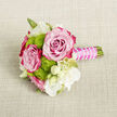 A delicate mini-bouquet lies on a softly textured, light beige fabric backdrop, the neutral tone of linen or burlap allowing every petal and ribbon to stand out. At its heart are two sumptuous roses, fully bloomed, their petals unfurling in tight spirals from pale blush at the centre to a richer fuchsia or magenta at the tips, capturing that fleeting moment of peak freshness. Around them, bright lime-green button chrysanthemums cluster like cheerful buttons, their rounded, densely petalled faces bringing a lively contrast and a modern note to the otherwise classic romance of the design. Weaving between these main blooms are slender white flowers and creamy buds, possibly small lisianthus or freesia, their fine petals and soft centres adding an airy lightness and a feeling of purity. A few thin, fresh green stems and leaves anchor the arrangement, giving it an organic, garden-inspired character, as if freshly gathered from a hidden courtyard off Stanmore Hill. The stems are neatly bound into a short handle and expertly wrapped in a smooth, satin fuchsia ribbon that echoes the deeper tones of the roses. Over the ribbon, a delicate garland of tiny white pearl-like beads winds in an elegant spiral, catching subtle glints of light and introducing a touch of bridal jewellery charm to the piece. The result is a refined, handcrafted boutonniere or petite bouquet, ideal for weddings, proms, or intimate celebrations in and around Stanmore, evoking soft romance, careful attention to detail, and the artistry of an experienced local florist.