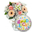 A cheerful good-luck gift set arranged against a clean white backdrop, captured as if on a bright morning in Stanmore. To the left, a generous bouquet sits in a clear glass vase tied simply with rustic twine; the waterline and vase curves are visible, letting the soft stems breathe. The flowers are a gentle celebration in peach and pink: powdery light-pink roses with tightly furled petals, silk-smooth peach-orange Gerbera daisies with dark brown centers, and tiny clusters of crisp white and lime-green chrysanthemum florets that add a fresh, lively texture. Wisps of delicate white baby's breath (gypsophila) float through the arrangement like lace, while deep green foliage frames the blooms and gives the composition depth. In the right foreground, slightly overlapping the lower vase, a round metallic silver foil balloon reads Good Luck! in a playful, multicoloured font; the letters bounce in green, orange, red and blue, and the two o's in Good are bright yellow smiley faces-one winking, one sticking its tongue out-adding a mischievous, hopeful expression. Scattered hearts, stars and confetti shapes in pink, blue, yellow and green catch the light on the balloon's sheen. The overall scent suggests soft rose perfume tempered by the clean, green lift of chrysanthemums and foliage. As a local florist imagining this for a friend leaving for university or an interview, I see a gift that radiates gentle encouragement and quiet celebration - ideal for same-day delivery across Stanmore High Street and nearby Bentley Priory when someone needs a little extra luck.