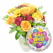 A bright, comforting Get Well Soon gift ensemble captured against a clean white background: on the left a lush bouquet of fresh garden-style flowers in a clear glass vase, and to the right a shiny round Mylar balloon bearing a cheerful message. The bouquet centres on several large, softly unfurling roses in warm orange and deep yellow tones; their velvety petals catch a soft, morning light and suggest a gentle citrus-tinged scent. Scattered among the roses are sunny yellow gerbera daisies whose open faces add instant cheer, while ruffled, deep burgundy carnations give the arrangement texture and visual weight. Delicate sprays of white alstroemeria thread between the bolder blossoms, introducing lightness and a whisper of sweetness, and abundant glossy green foliage frames every stem for a fresh, lively silhouette. The vase is transparent, showing water and the network of stems beneath, which grounds the composition with honest florist craftsmanship. Nestled partially in front of the bouquet, the metallic silver balloon reflects the studio light and serves as a playful backdrop: a central cluster of cartoon-style balloons in blue, purple, green, pink and yellow-some patterned with stripes, dots and checkerboards-surrounds bold yellow-and-blue letters that read Get Well Soon with a soft shadow for depth. Small starburst accents and a tiny KALEIDOSCOPE logo at the bottom edge complete the happy design. This pairing reads as a thoughtful bedside or bedside-table gift-ideal for sending sunny, reassuring wishes to someone recovering in Stanmore or nearby wards like the Royal National Orthopaedic Hospital, carrying the warmth of a local florist's care.