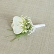 A single white orchid boutonniere rests gently on a softly textured, light beige woven fabric, the kind of natural linen you might find in a quiet Stanmore bridal studio. At the centre, a pristine Phalaenopsis orchid bloom opens in serene, velvety curves, its broad white petals catching the soft, even light so they appear almost luminous against the neutral backdrop. Within its throat, a whisper of pale yellow and cream adds warmth, hinting at the living, breathing flower behind the polished design. Surrounding the orchid, countless tiny white baby's breath blossoms gather in airy clusters, like a delicate cloud encircling the main bloom. Their minute, cottony petals create a subtle halo, softening the outline and giving the boutonniere a weightless, romantic feel, reminiscent of a gentle mist hanging over Stanmore Common on an early spring morning. Threading through and beneath the flowers, fine strands of feathery green foliage stretch outward, their fresh, grassy tones offering a natural counterpoint to the cool whites. The greenery feels light and graceful, with a slightly wild line that suggests movement and life. At the base, the stems are neatly bound in a smooth white satin ribbon, wrapped tightly and finished with a small, understated bow that lies flat and refined, ready to be pinned to a groom's or groomsman's lapel before a ceremony at a local Stanmore church or registry office. The overall impression is one of quiet sophistication and timeless purity, a handcrafted floral detail that speaks softly but confidently of love, commitment, and the careful artistry that goes into every wedding flower created for couples across Stanmore and the surrounding north-west London neighbourhoods.