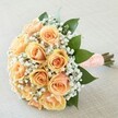 Softly illuminated, this elegant bouquet encapsulates the timeless beauty that Stanmore's florists bring to special occasions. Peach and apricot roses, gathered in a tight, harmonious cluster, bloom with a gentle luminescence-petal edges kissed with creamy blush, while their centres radiate deeper apricot hues, much like the treasured sunset views over Stanmore's leafy hills. Encircling the roses, feathery gypsophila creates a lace-like halo, their tiny white blossoms reminiscent of the delicate textures found in Stanmore's historic gardens. Framed by broad, glossy green leaves, the bouquet finds depth and a sense of renewal, echoing spring's arrival in the area's many green spaces. The stems, bound with a wide peach ribbon adorned with perfectly aligned pearls, offer smoothness and grace in the hand. Resting on a finely woven, neutral background, the bouquet glows in natural light, exuding quiet confidence and tender emotion-a composition perfectly suited for a wedding, anniversary, or cherished gathering in NW7. Every element in this bouquet evokes a fresh start, deep joy, and the promise of a beautiful day shared in Stanmore's warm community.