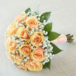 There is a refined tenderness to this arrangement: peach-hued roses gathered into a perfect, rounded bouquet, each bloom chosen for evenness of shape and the creamy gradient across its petals. Wisps of white gypsophila are artfully interspersed, their tiny blossoms softening the roses and creating an airy, romantic veil that breathes between the larger flowers. Rich, emerald-green foliage provides structure and contrast, glossy leaves folded and placed to frame the face of the bouquet and direct the eye toward its warm centre. The bouquet is finished with stems tightly wrapped in a textured, blush ribbon studded with pearl pins, a handcrafted touch that reads as both personal and timeless. Shot in gentle daylight that flatters the pastel palette, the arrangement gives off a subtle sheen and the impression of light from within. The scent is restrained and fresh: the clean, green notes of recently cut foliage mingle with the pale, honeyed sweetness of the roses and the faint, powdery perfume of gyp. Prepared with the care of a local workshop and often requested for weddings and vow renewals near Stanmore station and Canons Park, this style is exactly the kind of thing we create at Flowers Stanmore when clients ask for classic, understated romance. It carries an air of anticipation and quiet joy-an elegant keepsake that feels handmade, considered, and perfectly suited to cherished moments in and around our neighbourhood.
