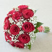 An opulent yet understated bouquet of red roses and white baby's breath rests in soft daylight, the kind that might filter through a Stanmore bay window overlooking leafy streets. The roses command attention first: deep crimson blooms, fully open but still pristine, each petal folding outwards with a satin-like sheen. Their rich colour speaks of devotion and celebration, creating a focal point that feels both grand and intimate. Interwoven among the roses, airy plumes of white gypsophila float like gentle clouds, offering contrast and a sense of grace, the way light drifts over Stanmore Common on a clear morning. Small touches of fresh green foliage peek from under the flowers, providing structure and a natural frame that subtly enhances the reds and whites. The bouquet is clearly hand-tied with care, its stems gathered into a smooth, comfortable handle, wrapped in a carefully chosen ribbon and adorned with a delicate line of pearls that glimmer softly, evoking bridal buttons or a cherished heirloom bracelet. If you could hold it, the bouquet would feel substantial yet easy to carry, the roses firm and weighty, the gypsophila feather-light to the touch. The imagined scent is gentle but romantic: a classic rose fragrance, sweet and full, lifted by the fresh, almost airy notes of the baby's breath. The overall impression is one of poised celebration-an arrangement perfectly suited for a Stanmore church wedding, a registry office ceremony near The Broadway, or an intimate anniversary meal at home, lovingly prepared and ready for same-day delivery to couples marking a special chapter in their story.