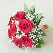 Classic red rose and baby's breath bouquet lying on an off-white, textured fabric surface, the neutral tone acting as a subtle stage for the rich colours of the flowers. At the heart of the arrangement, several fully opened red roses-deep crimson in shade-form a compact, rounded cluster, each bloom showing its layered, velvety petals curling gently outward. Nestled among them, fine stems of white gypsophila weave in and out, creating airy, cloud-like pockets of tiny blossoms that lighten the overall look and highlight the intensity of the red. Around the perimeter, lush dark green leaves, smooth and slightly pointed, extend from beneath the blooms, giving the bouquet a full, domed shape and a fresh, just-crafted feel. The stems are bound together in a tight, elegant bundle, wrapped in wide red ribbon that matches the roses, the handle finished with a row of small pearl-like decorations positioned in a delicate spiral along the ribbon. The lighting in the image is soft and even, gently highlighting the curves of each petal and the fine detail of the gypsophila without casting harsh shadows. This is the kind of hand-tied design you might see carried at a Stanmore wedding, photographed outside a local church or along The Broadway, or presented as a romantic gift for a special dinner at home. It communicates love, formality, and classic taste, a bouquet designed for moments that truly matter.