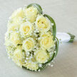 This elegant hand-tied bouquet, pictured from just above, showcases a classic cluster of roughly fifteen to twenty creamy yellow roses arranged into a full, rounded dome that suggests both opulence and restraint. The roses are a soft ivory-cream, petals unfurling in delicate spirals toward luminous centres; tucked between them, sprays of tiny white Gypsophila (baby's breath) float like mist, softening the composition and adding a light, romantic texture. Threads of vibrant green bear grass or lily grass have been woven and curved around the outer edge, their slim, arching shapes forming a subtle frame that lifts and defines the bloom cluster. At the base the natural green stems are neatly gathered and wrapped in smooth white satin ribbon, the handle finished with a tidy knot that feels comfortable to cradle. The bouquet rests on a pale off-white linen surface, and the soft, diffuse light in the photo reveals gentle tonal shifts across the petals and a fresh, dewy suggestion to the scent. As a local florist in Stanmore, I picture this arrangement arriving for a bride preparing at a nearby home off Stanmore Broadway or being carried to a ceremony near Canons Park; Flowers Stanmore prepares this style for intimate weddings, anniversaries, and refined celebrations, with local delivery available across the Stanmore area. The mood is pure, serene, and slightly nostalgic - a timeless design that radiates quiet joy and considered craftsmanship.