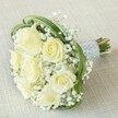 There is a subtle poetry in this bridal bouquet, thoughtfully composed on a soft beige textile that calls to mind Stanmore's tranquil residential streets and leafy parks. At its centre, eight creamy white roses reveal layer upon luminous layer-each bloom radiating calm and softly catching the light, as if capturing a moment of quiet hope. Breathlike tufts of baby's breath gather around the roses, giving the bouquet a misty, ethereal quality that conjures memories of spring mornings on Canons Drive. Encircling the blossoms, ribbons of verdant bear grass weave in fluid loops, their dynamic lines adding modern vibrancy and a gentle touch of whimsy. The stems are expertly arranged and snugly bound with a silver-grey, pearl-adorned ribbon-its lustre softly gleaming and inviting to the touch. Fresh-cut ends peek from beneath the elegant wrap, grounding the arrangement in freshness and sincerity. With its gentle fragrance and balanced composition, this bouquet feels suited for a heartfelt exchange-whether carried down the aisle, celebrated in a Stanmore home, or remembered as a symbol of fresh starts and cherished friendships in this close-knit North West London locale.