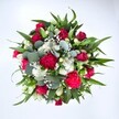From a clear, overhead view, this bouquet appears as a rich, circular pool of colour set against a pristine white background, every stem carefully placed to feel both full and balanced. Deep crimson red roses form the emotional core of the arrangement, some still tightly furled, others gently opening to reveal layered, velvety petals that hint at romance and quiet devotion. Around them, fuchsia and ruby red carnations unfurl in ruffled clusters, their plush, textured blooms introducing movement and a celebratory energy, like confetti frozen in floral form. Nestled between these warmer tones are crisp white spray chrysanthemums and other daisy-like white flowers, their neat petals creating bright, clean points of light that keep the composition feeling fresh rather than heavy. Tiny white gypsophila-baby's breath-drifts delicately through the bouquet, its cloud of minuscule florets softening edges and filling tiny gaps so that no harsh lines break the eye's journey. Framing all this colour is a lush collar of greenery: broad, pointed dark green leaves give structure, while rounded, silvery eucalyptus discs weave in and out, adding a cool, contemporary note and suggesting a gentle, aromatic freshness. The whole bouquet feels like a generous, hand-tied gift from an experienced local florist, the sort of arrangement you might have delivered to a loved one in Stanmore after a walk through Bentley Priory Nature Reserve, when you want flowers that say both I cherish you and let's celebrate. Ideal for birthdays, anniversaries, and heartfelt thank-yous, it radiates warmth, joy, and a sense of thoughtful care.