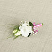 This photograph captures a lovingly arranged boutonniere resting on a light, textured background, the neutral fabric allowing each floral detail to stand out clearly. At the heart of the piece is a lush white lisianthus, fully open and delicately ruffled, its rounded petals layered in soft spirals that evoke a feeling of calm and gentle luxury. Two lisianthus buds, still mostly closed, lean affectionately into the main bloom, their creamy tones and elongated shapes adding harmony and balance. Between these blooms, fine stems of baby's breath weave through, each one topped with clusters of minuscule white flowers that create a misty, cloud-like effect. Threaded along one side and peeking from behind, slim green foliage introduces structure and a fresh garden feel, rather like the foliage you might see in the quieter gardens and parks around Stanmore. The florist has gathered all the stems together and bound them with a striking pink satin ribbon, its sheen catching the light, providing a contemporary note against the more traditional floral palette. The ribbon is wrapped tightly and finished in a small, tidy bow that adds a touch of personality-neither too bold nor too subdued. The soft lighting accentuates the contrast between the matte, slightly textured fabric beneath and the smooth gleam of the ribbon, as well as the velvet-like surface of the lisianthus petals. This boutonniere looks ideal for a wedding or elegant celebration in Stanmore, something that could be delivered fresh for a groom or guest, carrying with it an understated sense of joy, romance, and thoughtful preparation by an experienced local florist.