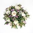 An overhead view reveals a round, hand-tied bouquet laid against a spotless white background, the clean surface making every petal and leaf stand out in crisp detail. At the heart of the design sit creamy white roses, their tones shifting gently from soft ivory to pale champagne, each bloom spiralling open in layered curls that suggest quiet luxury. Some roses are fully open, showing their intricate hearts, while others remain modestly cupped, giving the arrangement a sense of natural movement. Threaded between them are slender buds and blooms of deep purple and lavender alstroemeria, their petals streaked with fine markings and tipped with fresh green at the base, like the first hints of spring along the paths in Stanmore Country Park. Tiny white clouds of baby's breath float throughout the bouquet, their airy clusters softening the contrast between the richer tones and the dark, glossy foliage that frames the composition. The leaves are abundant yet carefully placed, forming a deep green halo that supports the flowers without overwhelming them, much like a well-kept garden on a quiet Stanmore side street. Soft, even lighting bathes the entire arrangement, eliminating harsh shadows and allowing every texture-from velvety rose petals to the slightly waxy alstroemeria-to be clearly defined. The bouquet feels refined yet welcoming, ideal for marking a wedding anniversary, sending gentle condolences, or simply brightening a home near Stanmore station. Its balance of classic white roses with contemporary purple accents speaks of calm sophistication and understated celebration, the kind of floral artistry a local Stanmore florist would send out for same-day delivery when someone wants to share comfort, admiration, or heartfelt affection.