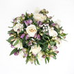 Seen from directly above, this sympathy bouquet appears as a softly rounded circle of flowers and foliage placed on a pure white background, every detail clear and undistracted. At the centre, creamy white roses gather closely together, some fully opened in generous spirals of velvety petals, others partially closed, their hearts still sheltered. The petals transition from gentle cream and ivory at their edges into a subtle, warm peach tone deeper within, giving each bloom a calm, glowing quality. Between the roses run slender stems of purple alstroemeria in tight bud, their tapered tops stained with deep lavender and muted violet, then fading slowly into light green and a blush of pink at the base, evocative of delicate evening colours drifting across Stanmore's open spaces. A few buds have begun to part, revealing the faintest glimpse of striped inner petals, quiet hints of life and beauty yet to unfold. Fine branches of baby's breath thread their way throughout the bouquet, carrying clouds of tiny white blossoms that create a soft, misty veil over the arrangement, adding lightness and gentle movement. Around the outside, deep green foliage forms a protective ring, the leaves smooth, broad, and slightly glossy, holding the composition together in a balanced, dome-like shape. The overall mood is gentle, dignified, and comforting-a bouquet that seems to breathe calm into a room. Designed in Stanmore with consideration for local traditions and family gatherings, it would rest naturally beside a memorial candle, on a service table, or in a quiet corner at home, offering a tender, enduring expression of sympathy.