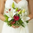 This Stanmore bridal bouquet feels like a heartfelt embrace-romantic, natural, and alive with local artistry. The grand white lilies, satin-smooth and edged with gold, are at once pure and bold, echoing the joyful anticipation of the day. Between them, sumptuous red roses spiral tightly, their velvet richness radiating promises of enduring love. Pops of bright red from berry-like hypericum punctuate the lush arrangement, their cheery tones bringing energy and playfulness. Wisps of baby's breath and moss-green button accents lend a soft, whimsical air, while a foundation of glossy, broad leaves and delicate ferns conjure the freshness of Stanmore's gardens in early bloom. The bouquet is clasped with gentle care by the bride, her hands steady and hopeful in the soft glow of natural light. As subtle fragrances of lilies and roses weave together, the bouquet becomes not just an accessory but a living memory-crafted to celebrate new beginnings and the shared joy found at the heart of Stanmore weddings.