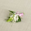 A delicately handcrafted boutonniere rests on a softly textured, light beige fabric, similar to natural linen, its neutral tone allowing every detail of the flowers to stand out. At the heart of the arrangement is a single white alstroemeria, or Peruvian lily, fully open so that its broad, slightly ruffled petals form a graceful star. Near the throat of the bloom, fine reddish-brown speckles and streaks create intricate markings that draw the eye inward toward the stamens, where a hint of pollen adds warmth to the white. Just to the left, a striking cluster of lime green buds, shaped like a narrow cone or floral spike, rises up with a tightly packed, scale-like texture, giving the piece a modern structure and a sense of fresh growth, much like the spring greenery in Stanmore's local gardens and quiet residential streets. Around these focal elements, dainty sprigs of white baby's breath float like tiny clouds, their numerous miniature blossoms softening the stronger shapes and lending an airy, romantic quality. A base of deep green foliage anchors the design: broader, sword-shaped leaves provide strength and contrast, while slender blades of bright green grass weave and curl, adding gentle movement and a natural, almost windswept feel. At the right side, the stems are neatly gathered and wrapped with a smooth, satin ribbon in clear, cheerful pink, tied into a compact bow that brings a celebratory note without overpowering the calm palette of white and green. The lighting is even and natural, highlighting each vein in the leaves and each petal edge, suggesting a freshly made piece ready to be pinned to a lapel for a wedding, prom, or formal event in and around Stanmore, capturing a quiet sense of joy and careful craftsmanship.