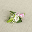 Resting on a pale oatmeal, woven-style fabric, this beautifully composed boutonniere captures the gentle charm of a Stanmore celebration. The focal point is a single, open white alstroemeria-type bloom, with soft, layered petals that curl slightly at the edges, showcasing slender reddish-brown markings along the inner petals that lead the gaze into the centre of the flower. Nestled closely around it are small white buds and partially opened blossoms, calling to mind tiny campanula or lily-of-the-valley flowers, each one suggesting a promise still unfolding. Fine sprays of white gypsophila thread through the arrangement, creating a light, cloud-like veil that lends the design a dreamy, romantic air suited to weddings near Stanmore Hill or intimate gatherings around local green spaces. To one side, an elongated, cone-shaped piece of vivid green buds, similar to ornithogalum, offers a striking vertical line and textural contrast, standing out crisply against the surrounding softness. Behind and beneath the flowers, broad, rich green leaves form a sturdy, glossy base, while slender ribbons of fine green foliage arc gracefully outward, echoing gentle movement like a breeze through the trees at Canons Park. The entire stem cluster is bound at the base with a glossy pink satin ribbon, tied into a neat, compact bow that adds a cheerful splash of colour and signals celebration without overwhelming the delicate blooms. The piece feels intentionally crafted and thoughtfully balanced, perfect for pinning to a lapel, dress, or wrist for a wedding, prom, or formal family occasion in Stanmore, where subtle elegance and heartfelt detail matter.