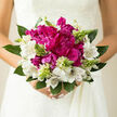 This photograph shows a hand-tied wedding bouquet that seems perfectly at home in Stanmore's leafy, peaceful surroundings. Dominating the centre are sumptuous magenta peonies, fully open and velvety, their many ruffled petals layered so densely that they appear almost like soft fabric rosettes. Their rich colour draws the eye first, offering a confident focal point that still feels romantic rather than bold. Framing these central blooms is a circle of white alstroemeria, each blossom gently flared, with slender petals carrying fine burgundy striations that add movement and subtle pattern, like delicate pen lines across crisp paper. Between the major flowers, slender stems of fresh green buds lift upward, some still tightly closed, others just beginning to reveal hints of petals within, suggesting the unfolding of a new chapter much like the start of married life in Stanmore. At the base, generous greenery curves outward, its cool green leaves overlapping in soft arcs that provide structure and a natural, garden-inspired feel, as if gathered from the borders of a home near Stanmore Hill or along the paths around Bentley Priory. The light is gentle and even, illuminating the bouquet without glare, allowing every texture-from the smooth leaves to the softly frilled peony petals-to be clearly seen. The imagined fragrance is light and fresh: a mix of crisp green stems and a soft floral sweetness, never overwhelming. The bouquet carries an air of thoughtful craftsmanship and emotional warmth, ready to be held by a bride stepping into a local church, registry office, or elegant Stanmore venue, marking the moment with flowers that speak quietly of joy, devotion, and shared promise.